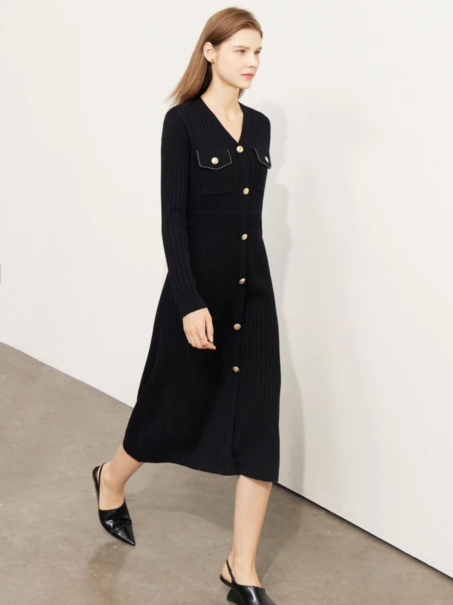 Model walking in black ribbed knit midi dress with gold buttons, long sleeves, and fitted silhouette