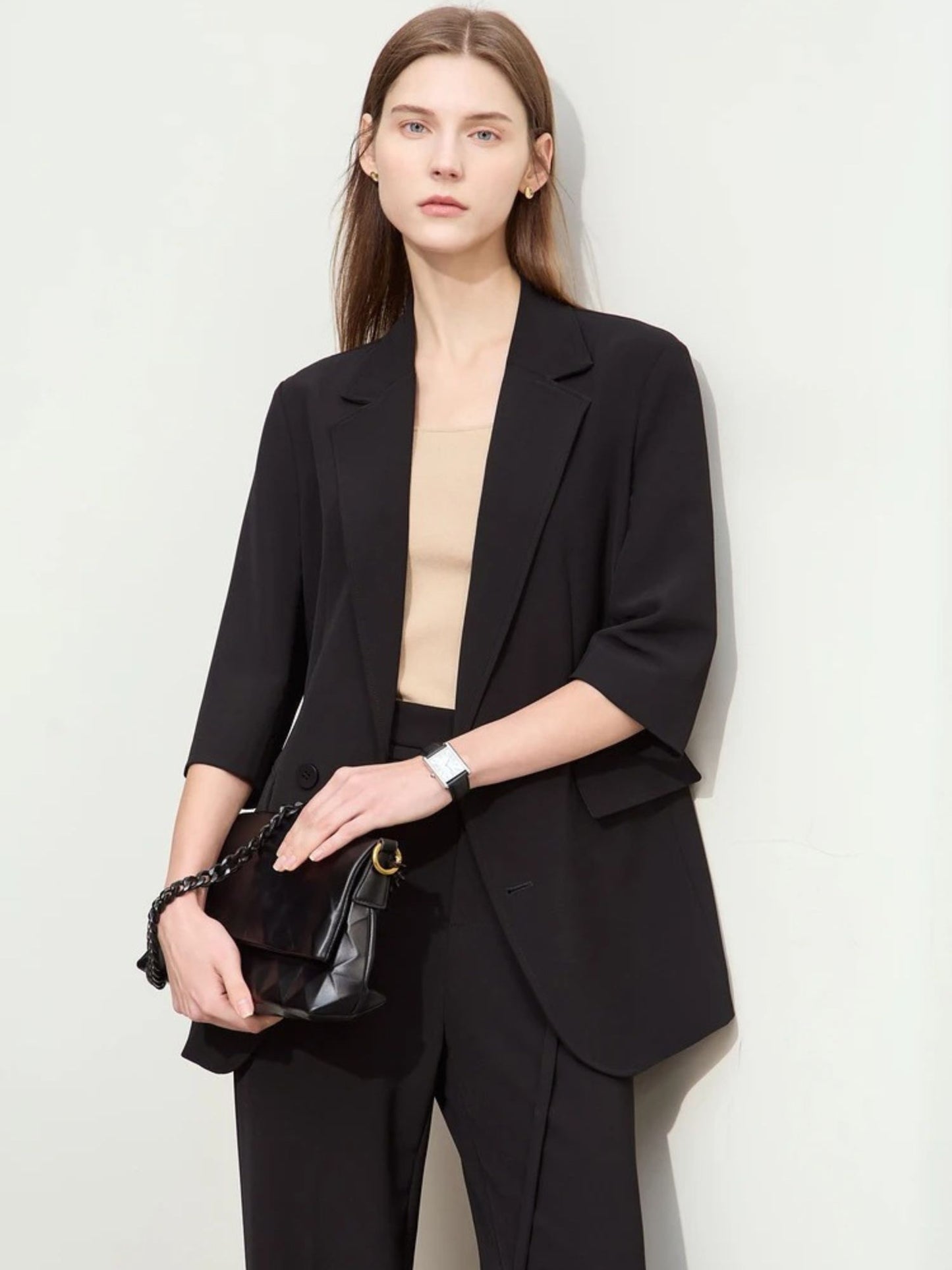 Close-up front view of woman in black elbow-length blazer and matching trousers with black accessories