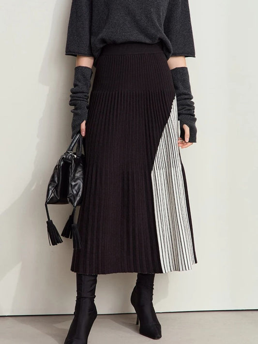 Black pleated midi skirt with asymmetrical color-block panel in light gray. Model wearing black top and tights