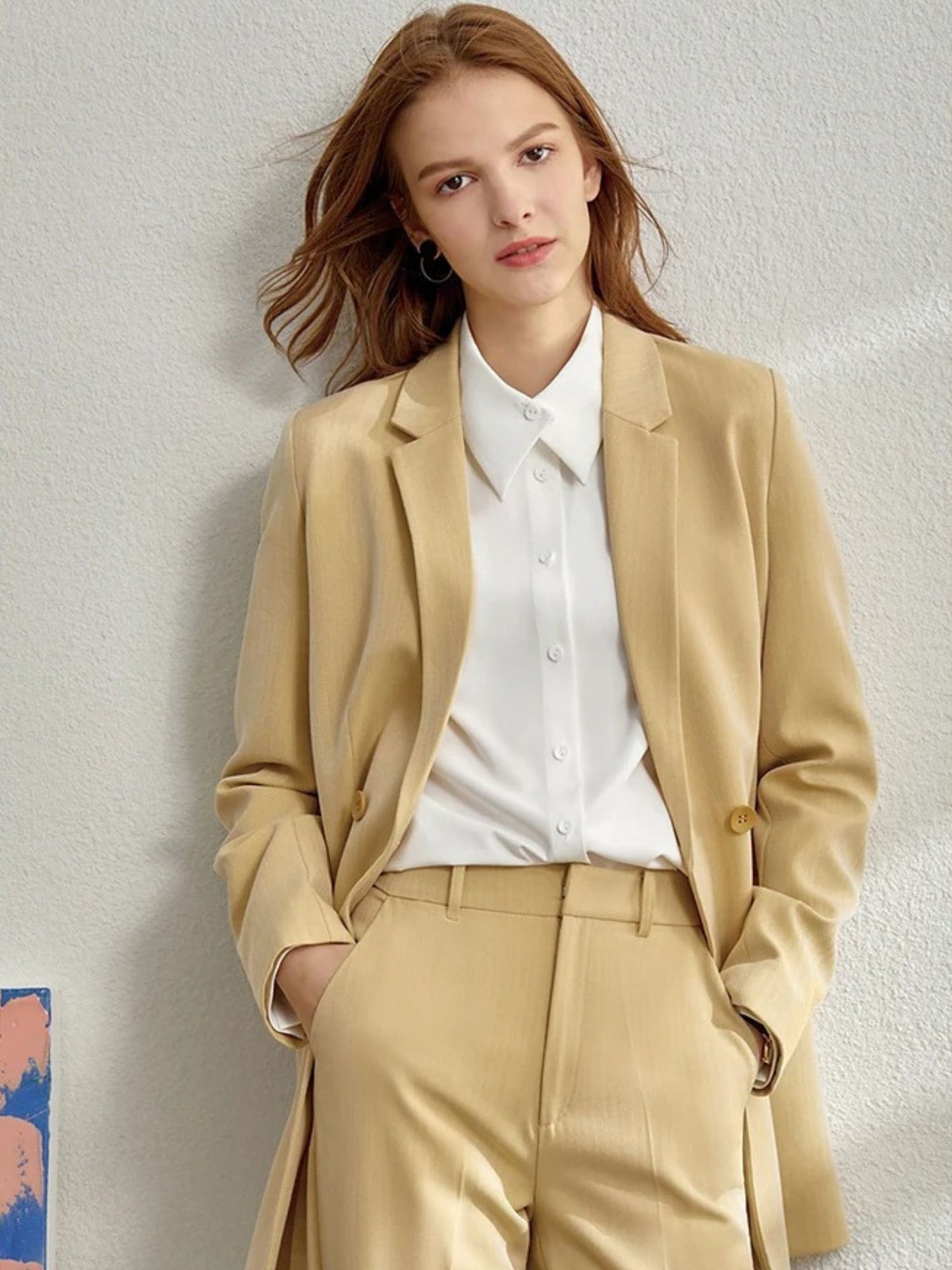 Model walking in beige pantsuit with soft drape, notched lapel, and light layering
