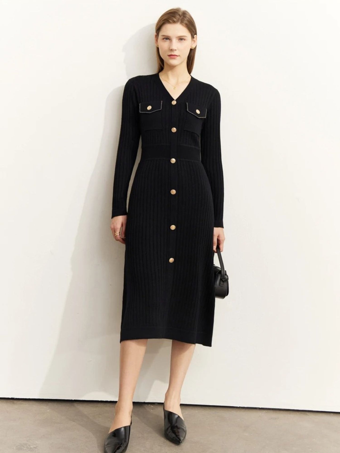 Women's black ribbed knit midi dress with long sleeves, gold button-front closure, and chest pockets. Model holding a black handbag