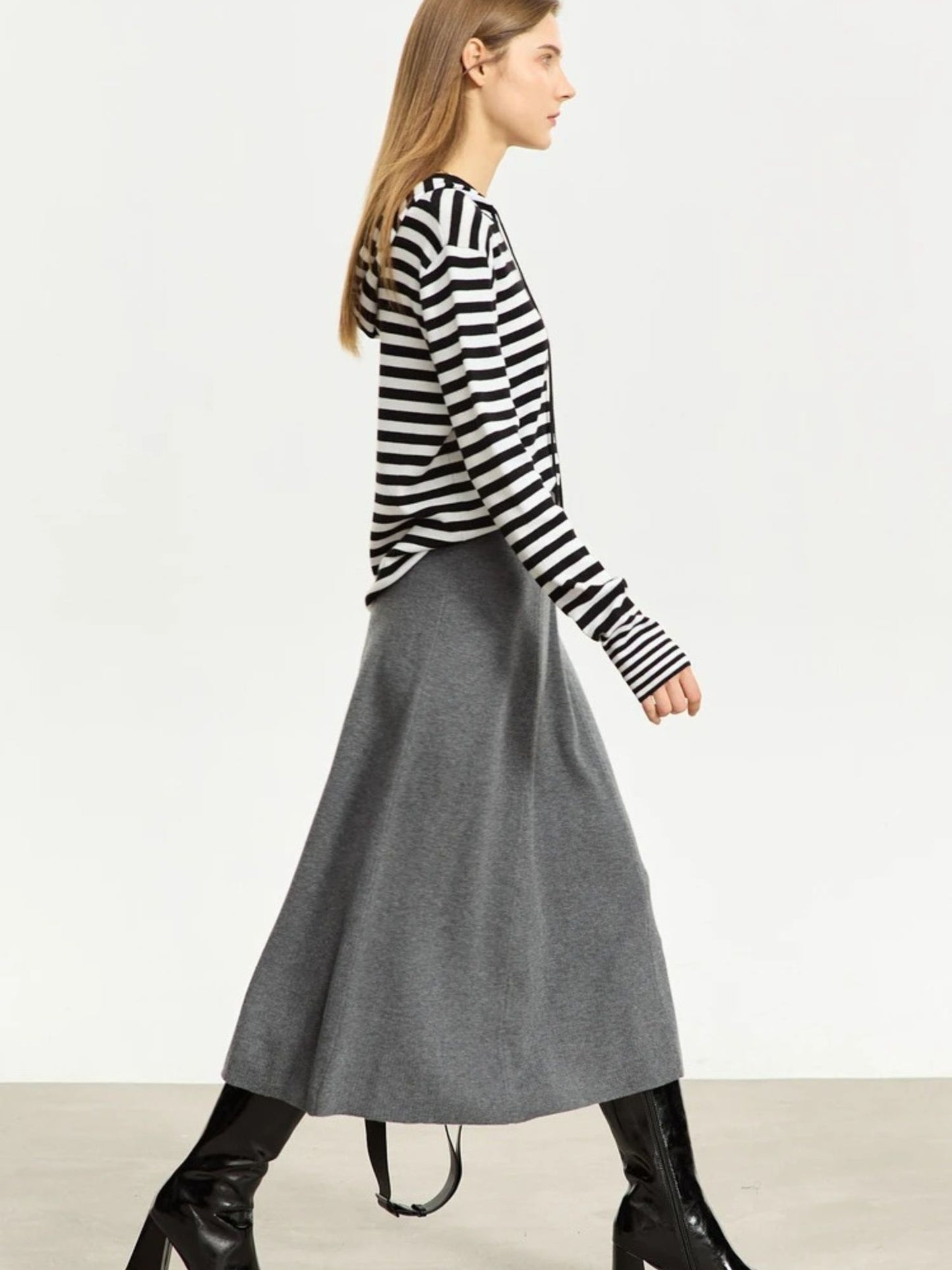 Woman wearing a black and white striped sweater with a gray skirt on a plain background