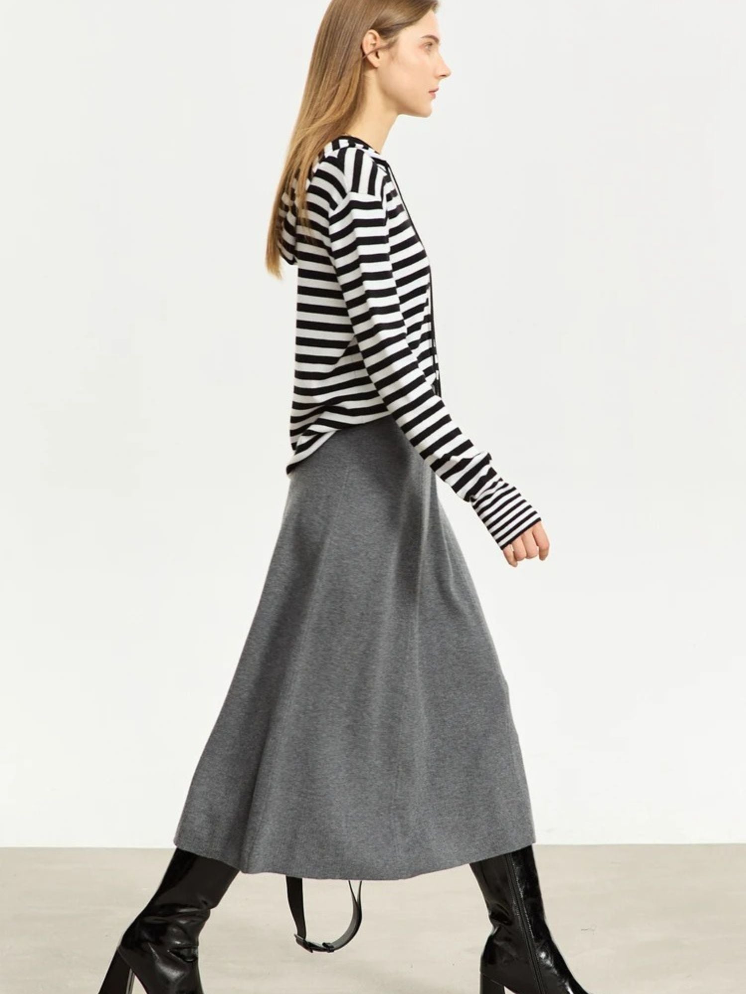 Woman wearing a black and white striped sweater with a gray skirt on a plain background