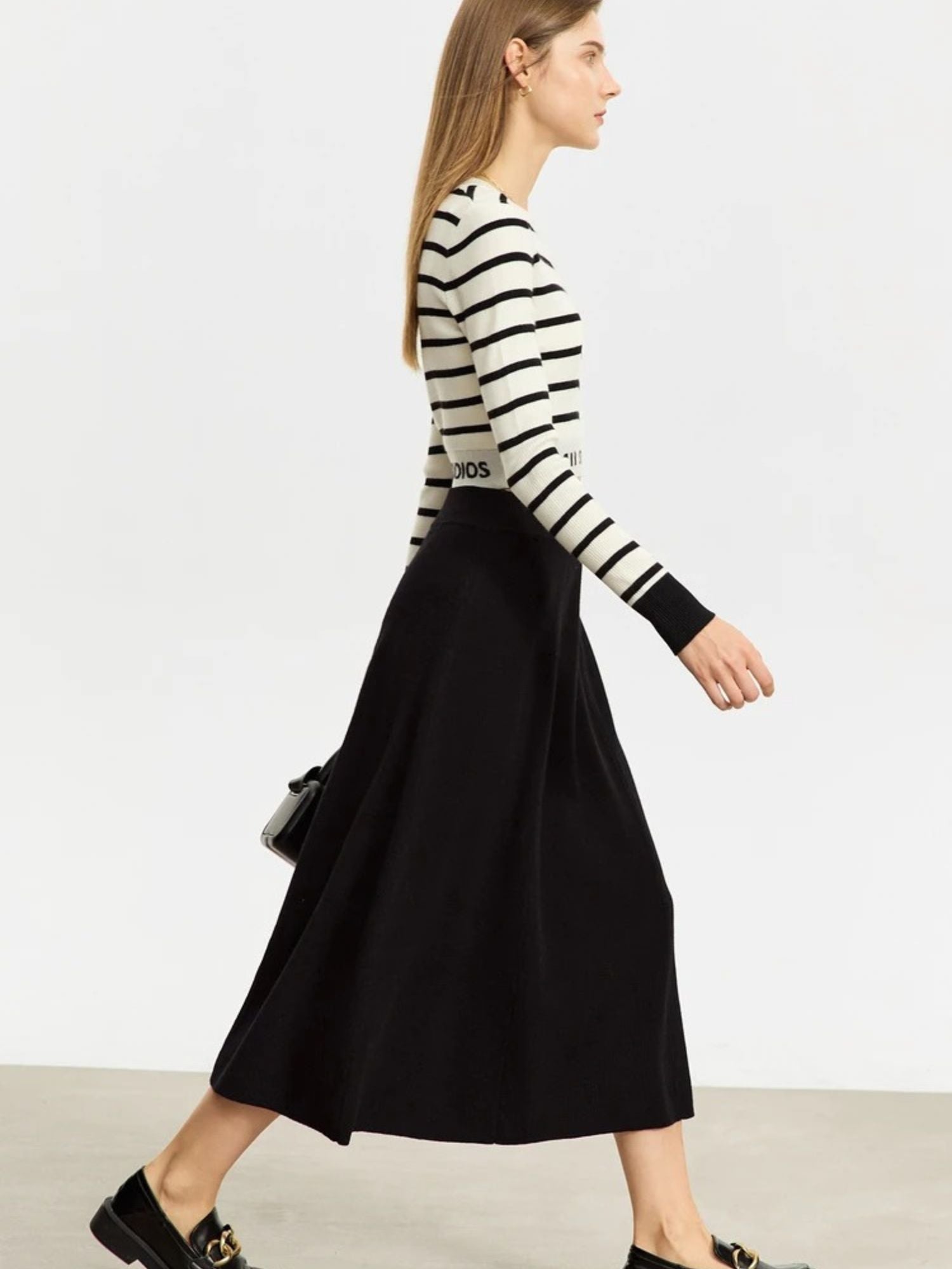 Woman wearing a black and white striped sweater with a brand logo and a black skirt on a plain background.