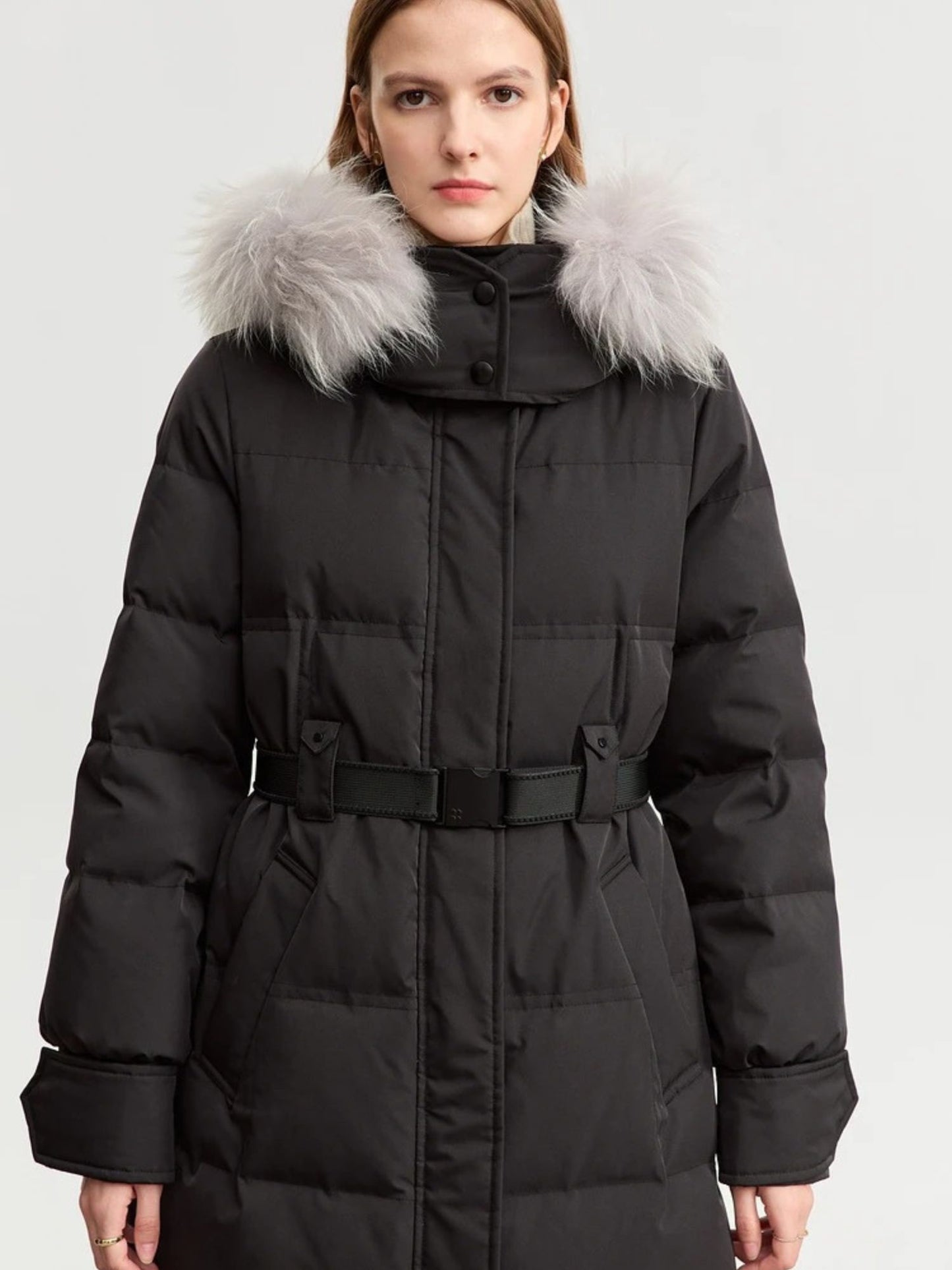 Black version of the coat, front view with fur trim on the hood. The model stands with hands in pockets
