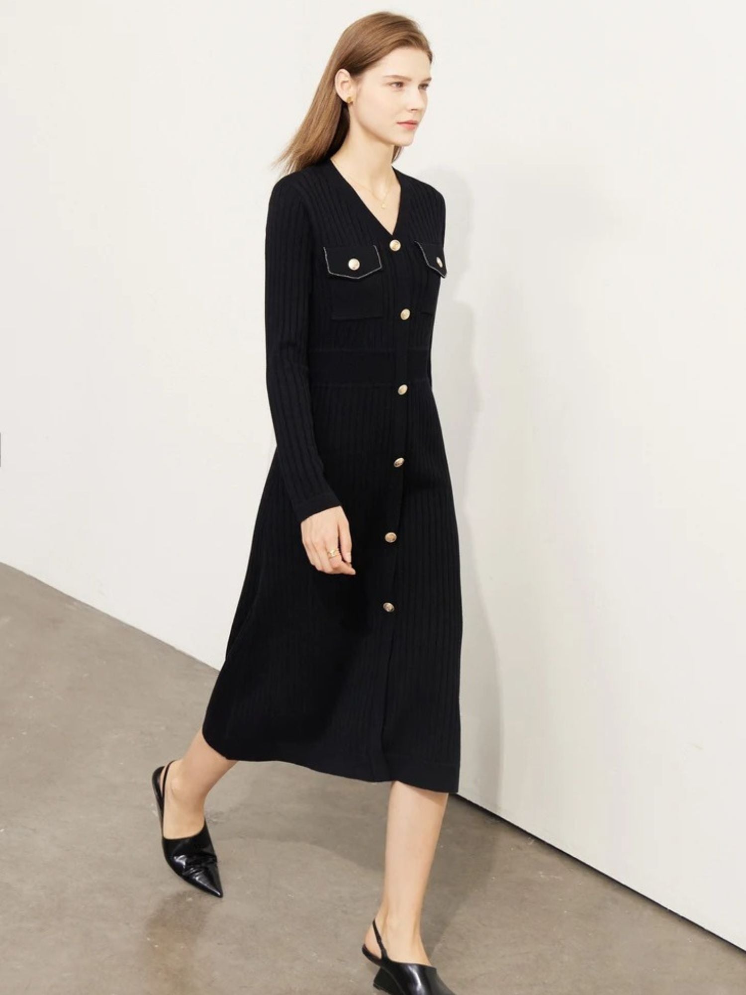 Model walking in black ribbed knit midi dress with gold buttons, long sleeves, and fitted silhouette