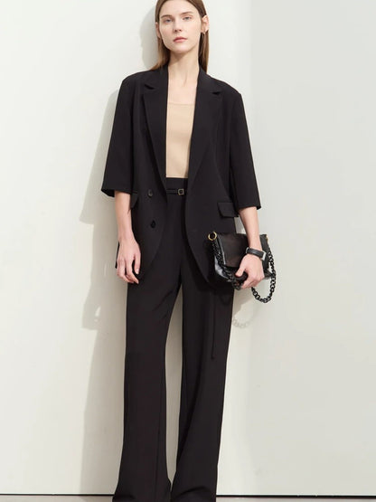 Front-facing woman in black wide-leg pants and elbow-sleeve blazer over a beige top, holding a black handbag