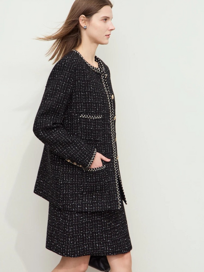 Side profile of the model in the black tweed jacket and skirt. Her hair is blowing slightly as she walks, showcasing the movement of the jacket