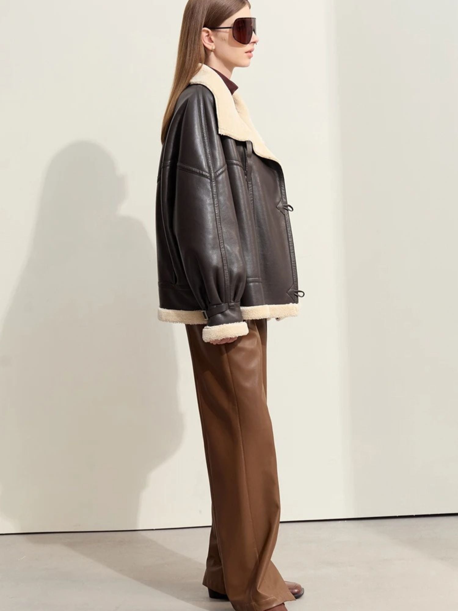 Side view of the model standing in a relaxed pose, looking to the right. The sleeve volume and jacket’s slightly boxy cut are evident