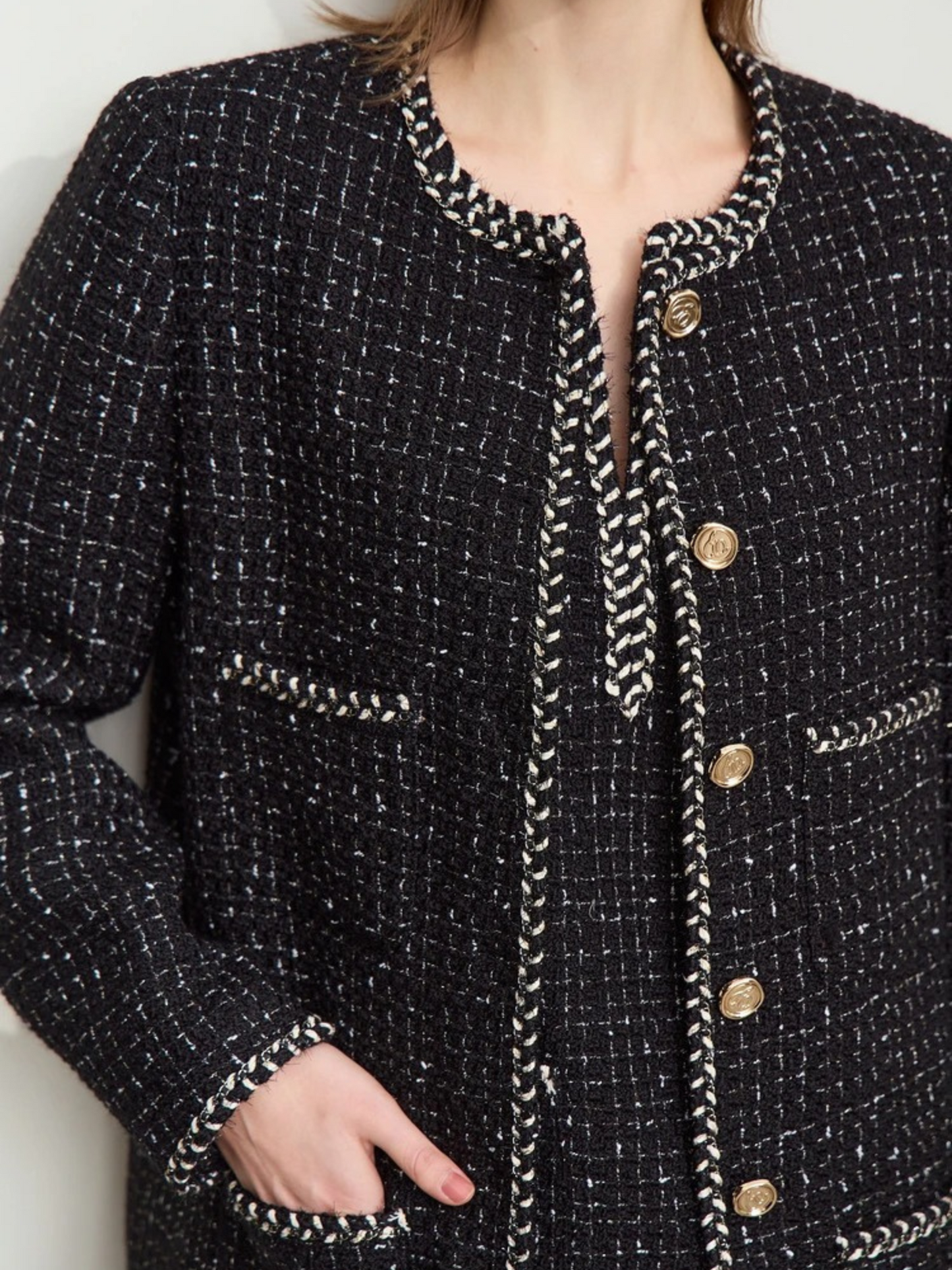 Close-up detail of the black tweed jacket, focusing on the gold buttons, textured fabric, and decorative trim around the pockets and edges