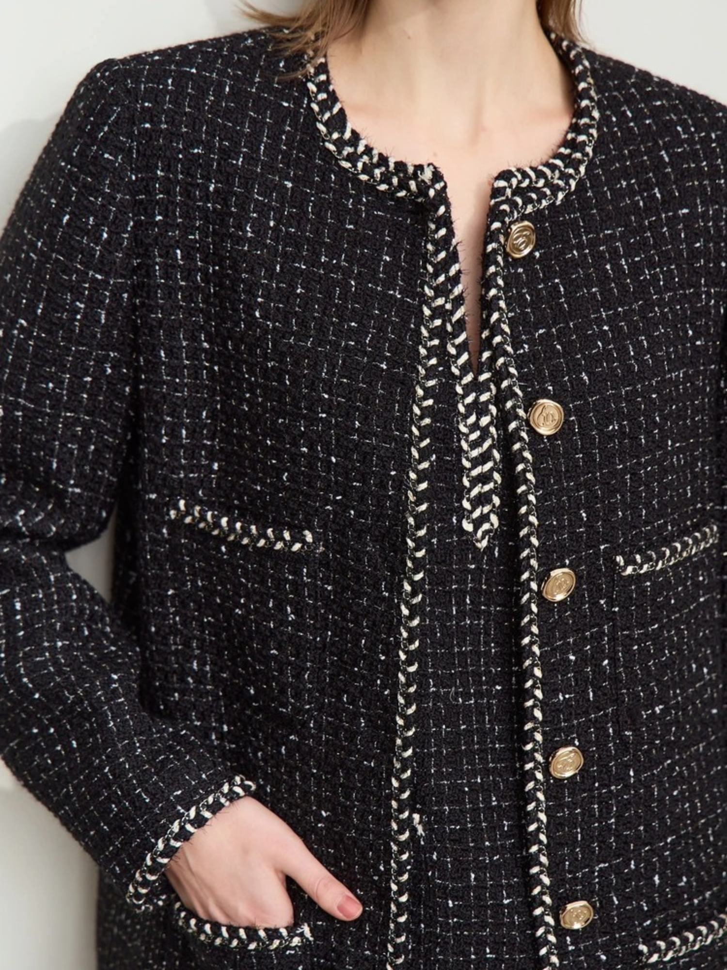 Close-up detail of the black tweed jacket, focusing on the gold buttons, textured fabric, and decorative trim around the pockets and edges