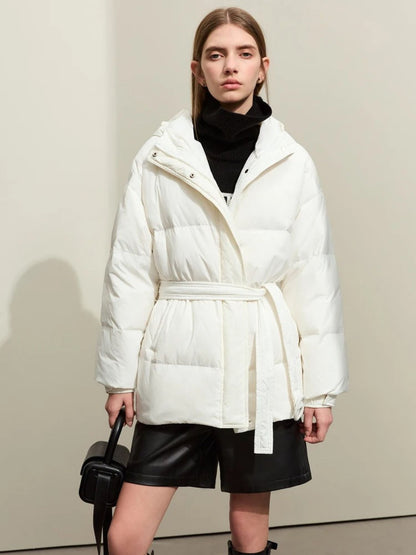 Model wearing the same puffer jacket design in white. She stands front-facing, with a black handbag, black shorts, and knee-high boots. The high neck and belt are clearly visible