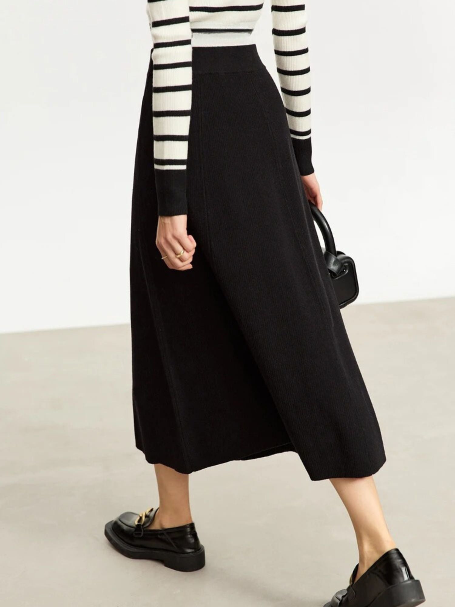 Person wearing a black skirt and striped sweater on a plain background