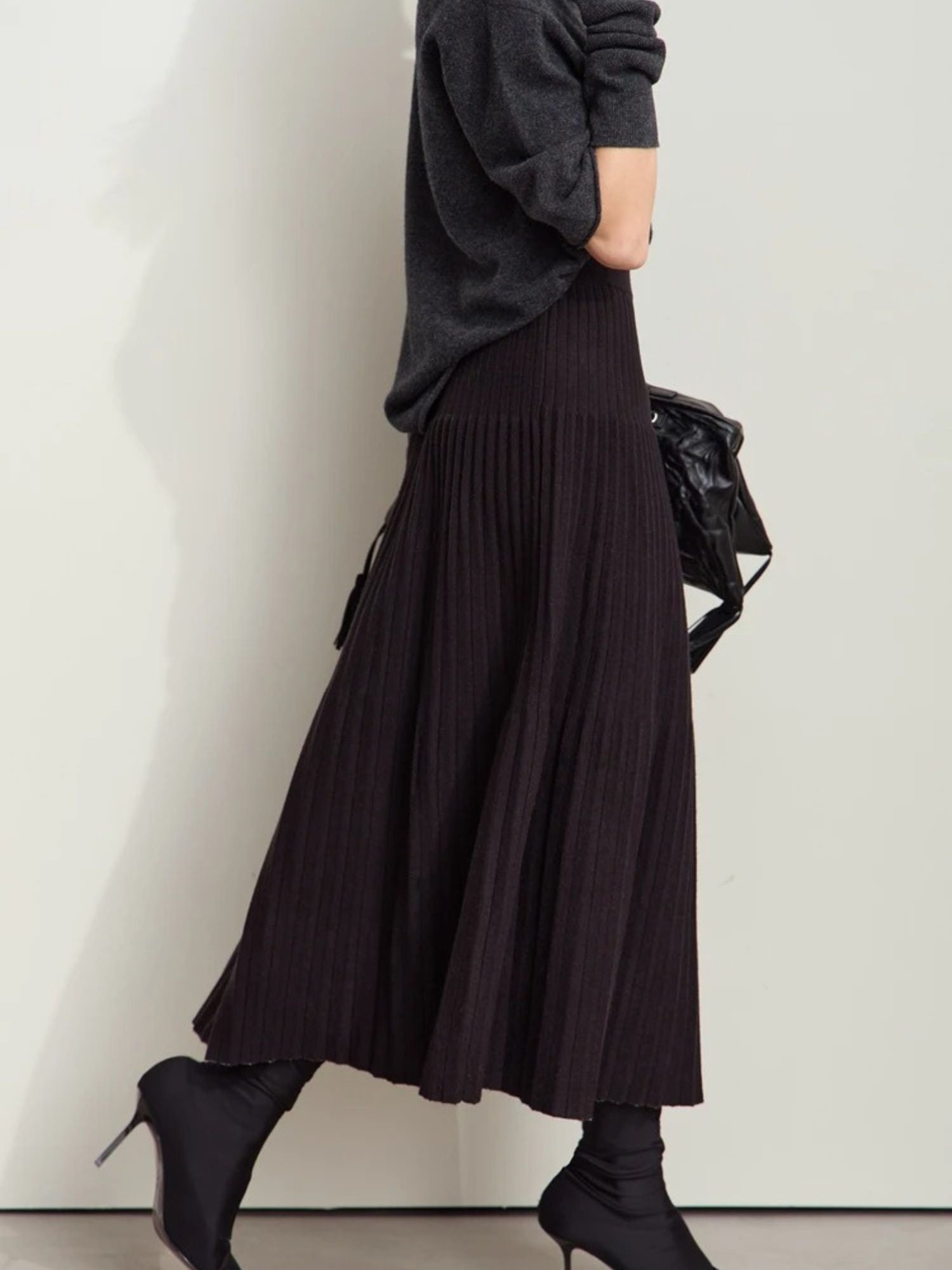 Model walking in black pleated midi skirt with light gray color-block panel, paired with black top and tights