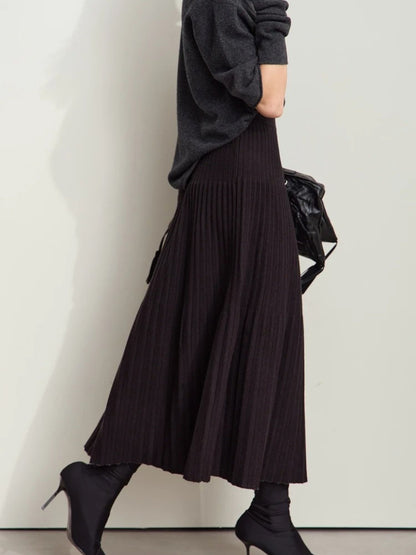 Model walking in black pleated midi skirt with light gray color-block panel, paired with black top and tights