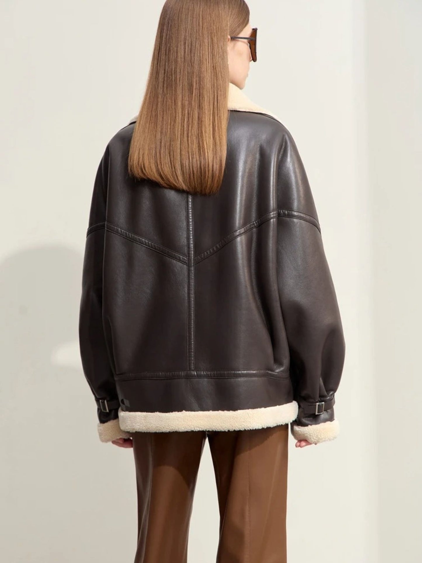Rear view of the jacket, showing the back panel, drop-shoulder seams, and shearling trim at the hem and cuffs. The jacket has a wide, boxy fit