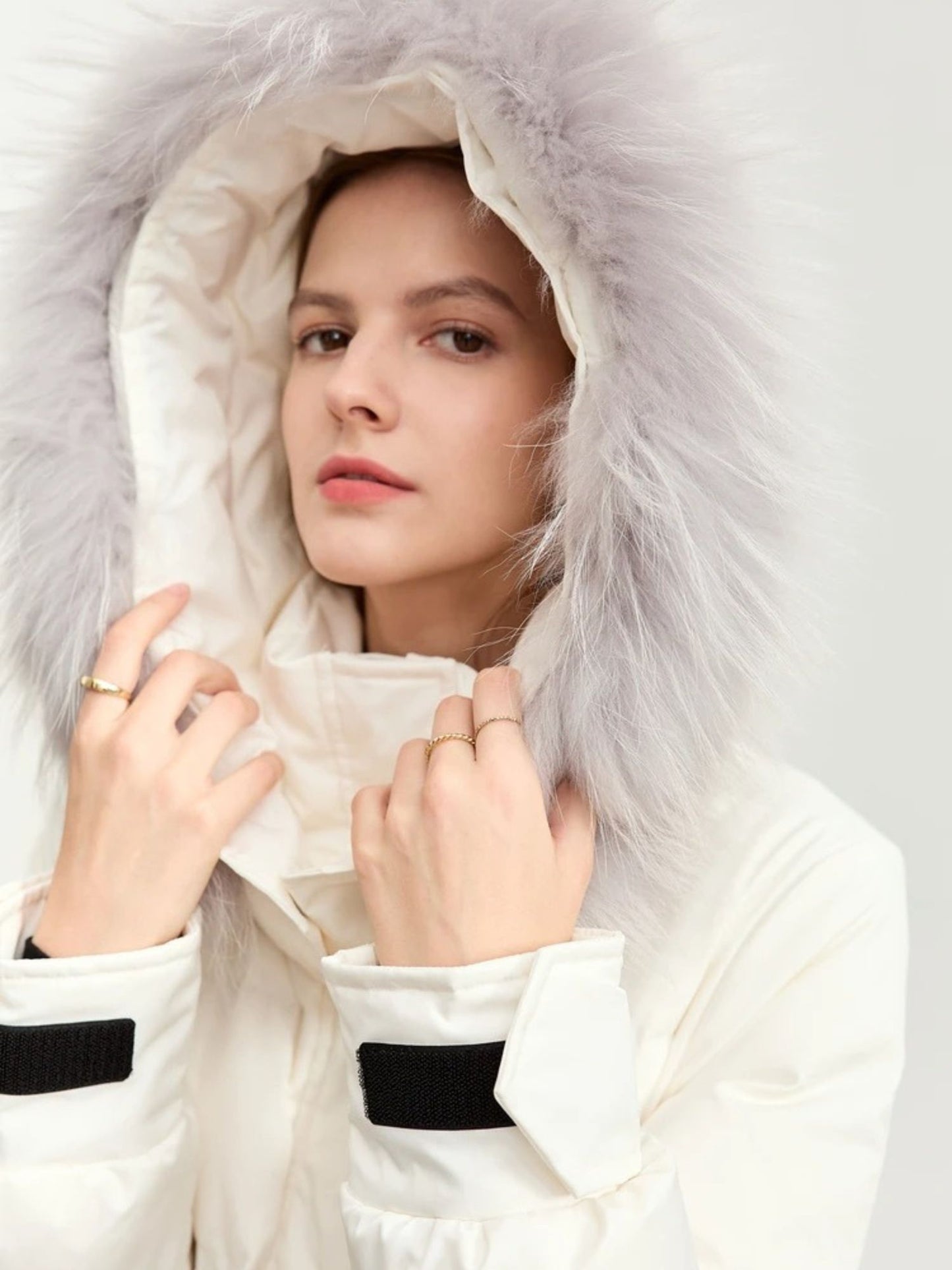 Close-up of the white coat's hood with fur trim. The model has her hands gently framing the hood, looking forward