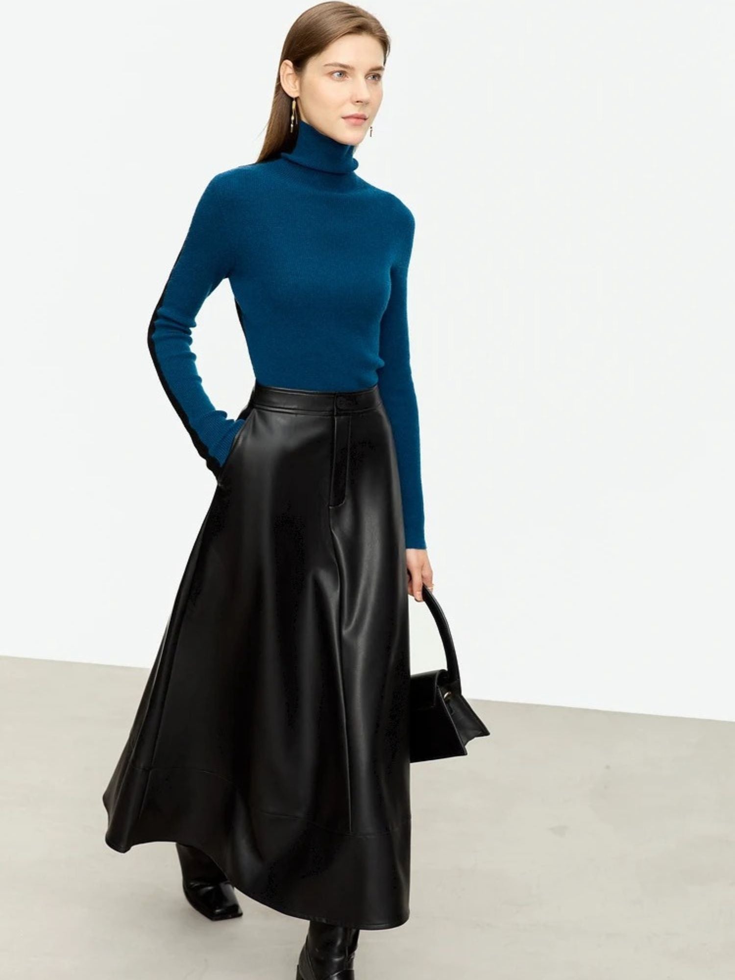 Model wearing black A-line faux leather midi skirt paired with fitted cobalt blue turtleneck and black boots