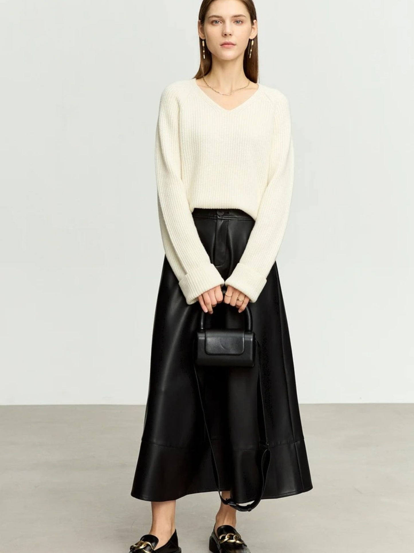 Black flared faux leather midi skirt styled with cream knit sweater and pointed heels