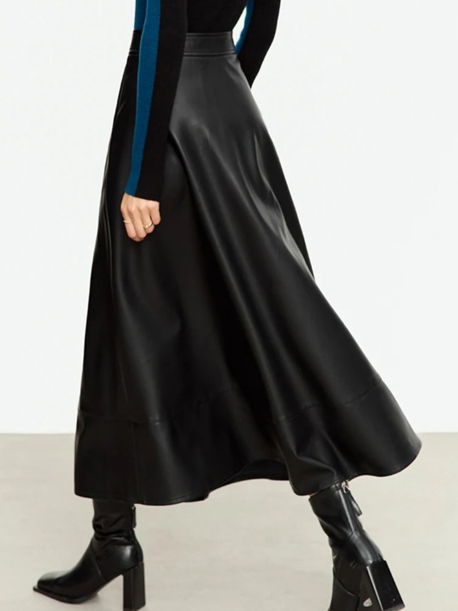 Black faux leather skirt in motion, styled with blue top and heeled boots for elegant look