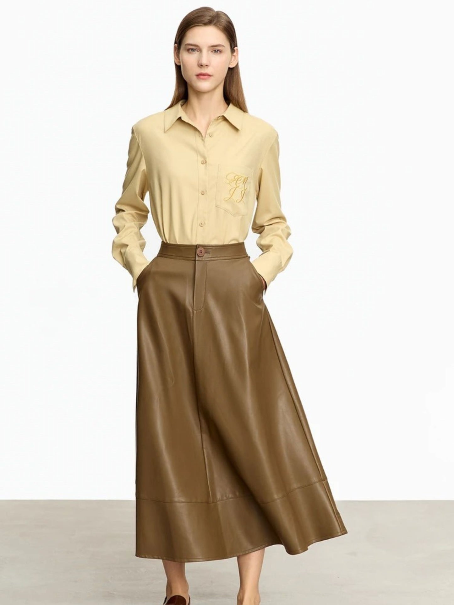 Brown A-line faux leather midi skirt paired with light beige blouse and neutral-toned footwear