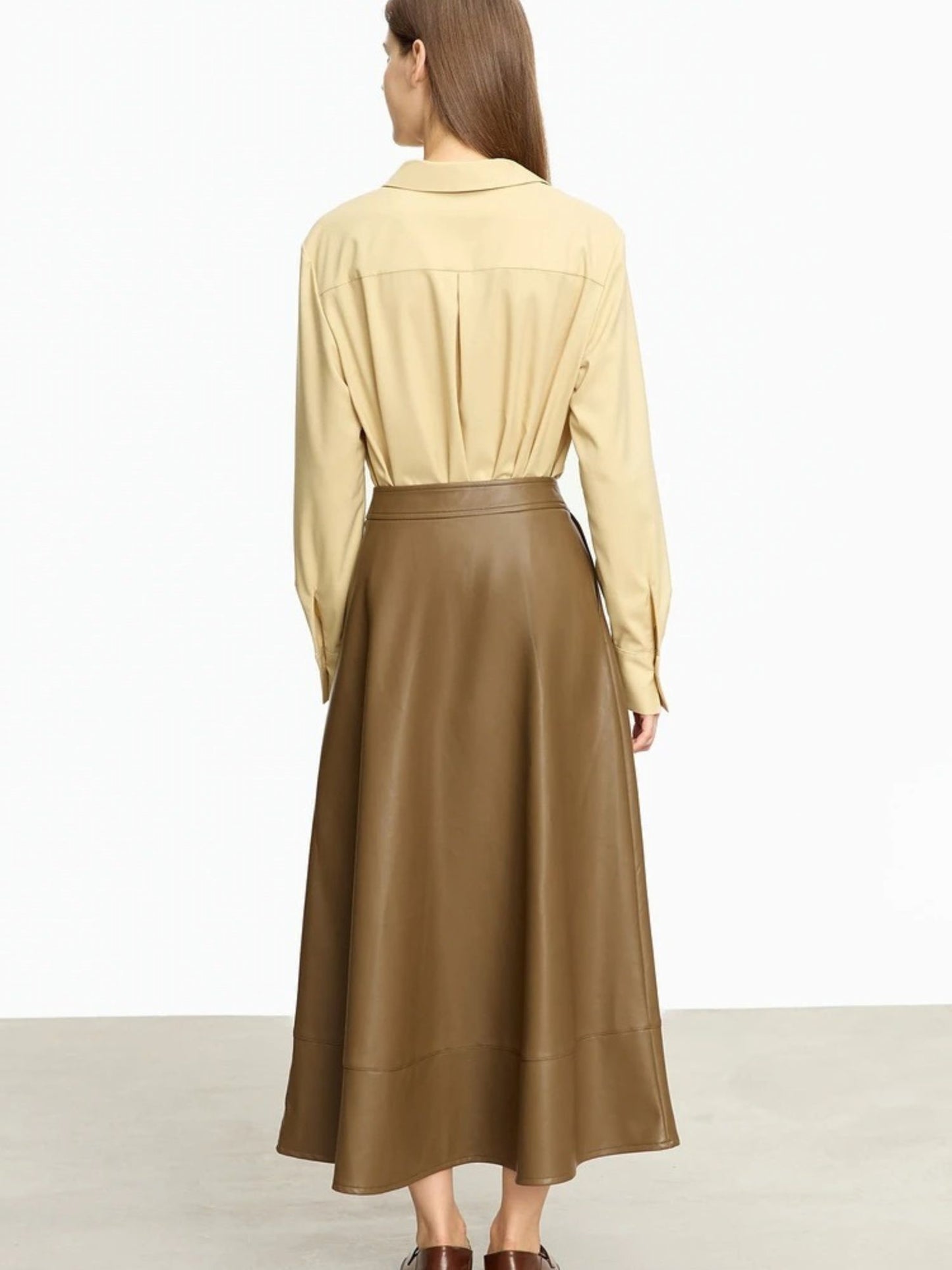 Back profile of brown faux leather skirt worn with tan blouse, showing clean seam and soft flare