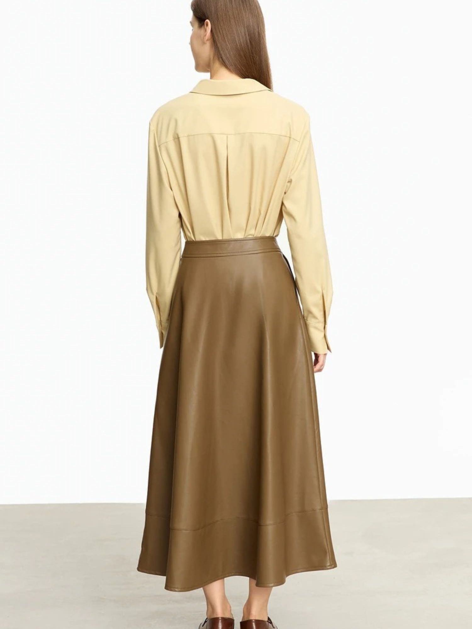 Back profile of brown faux leather skirt worn with tan blouse, showing clean seam and soft flare