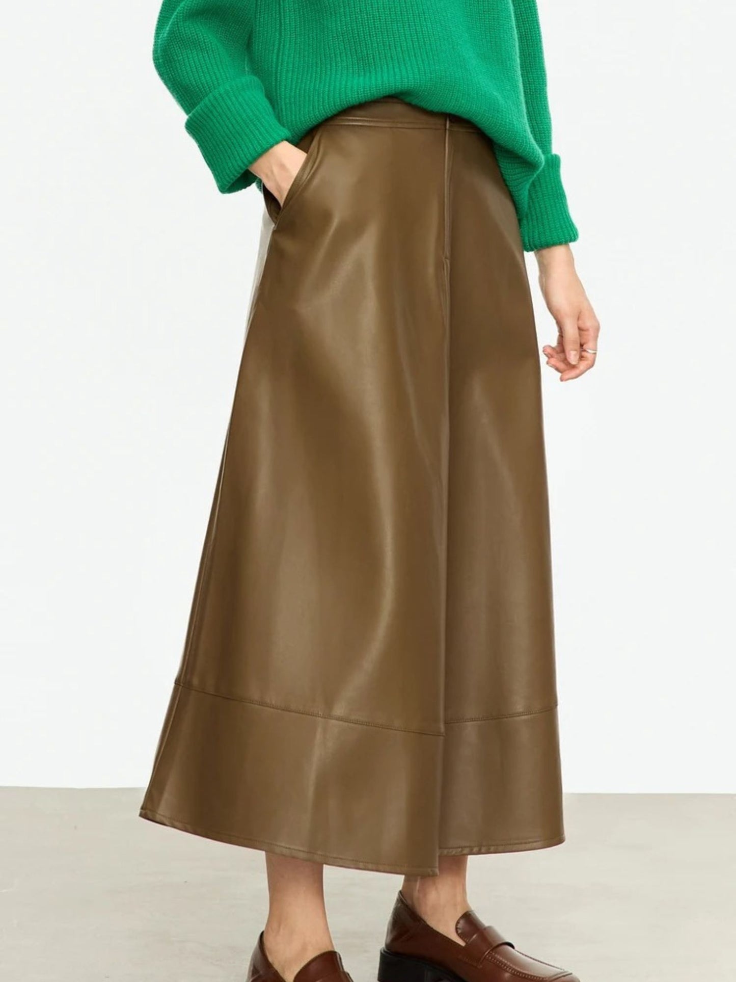 Side view of brown leather-look midi skirt styled with bright green top and low-heeled shoes