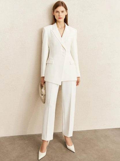 Model wearing structured white blazer with matching tailored pants, styled with pointed heels and clutch